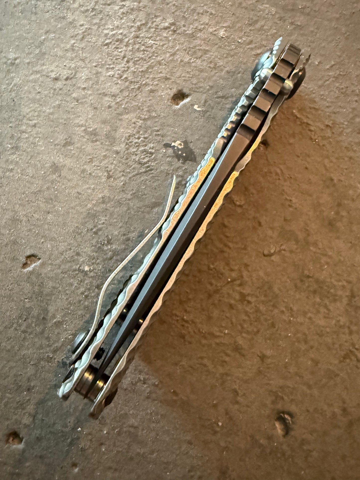 Rear spine view of Strider SnG full titanium DGG knife displaying black blade, open-back construction, pocket clip and Double Gunner Grip texture.