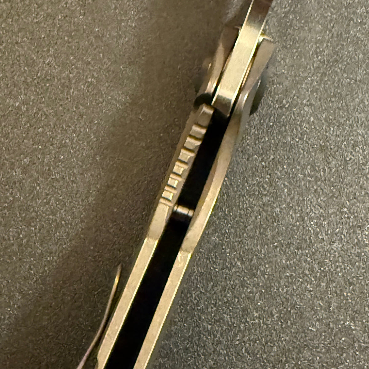 Close-up of Strider SnG CC compound grind knife showing blade spine, full Acid Bronze titanium scales, and open-back construction.