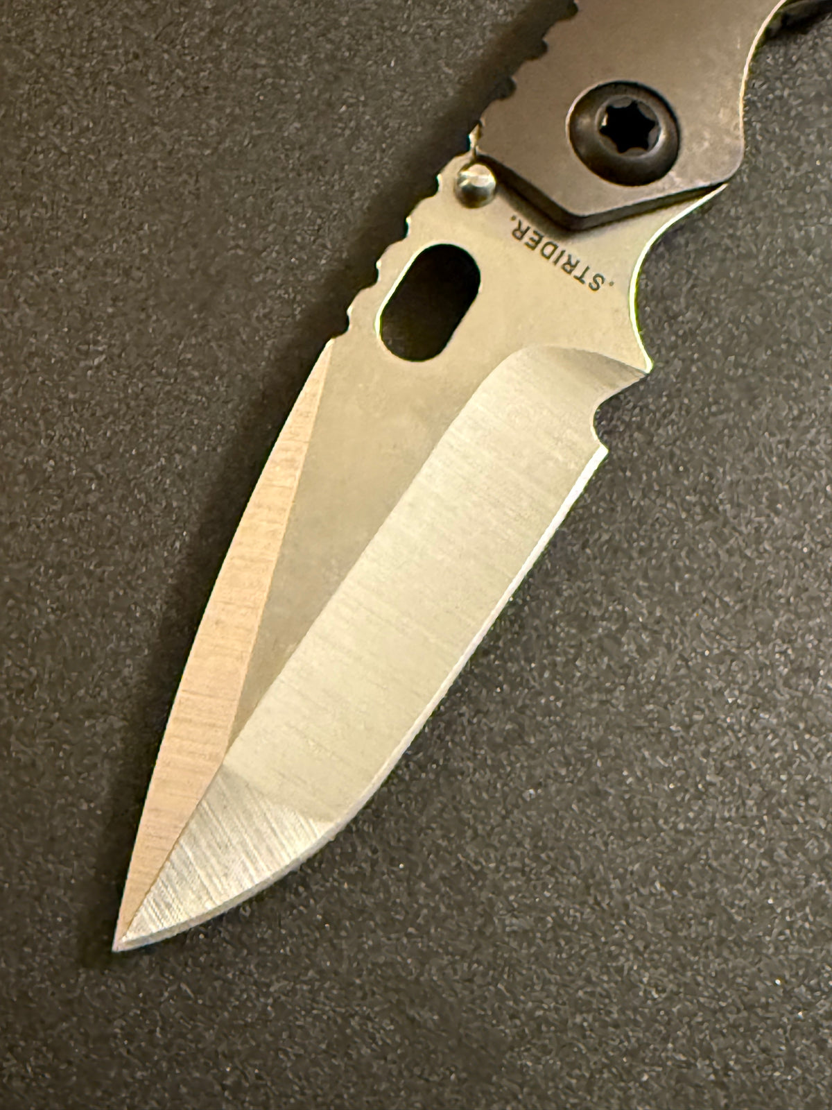 Detailed Strider SnG CC CPM MagnaCut compound grind blade with contrasting satin bevels, oval thumb opening, and Acid Bronze titanium handle.