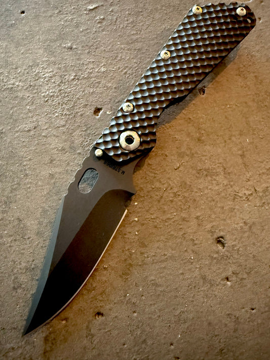 Strider SMF DGG full titanium folding knife with hand-ground PD1 Bowie blade, black PVD finish, Double Gunner Grip milling and upgraded titanium hardware.
