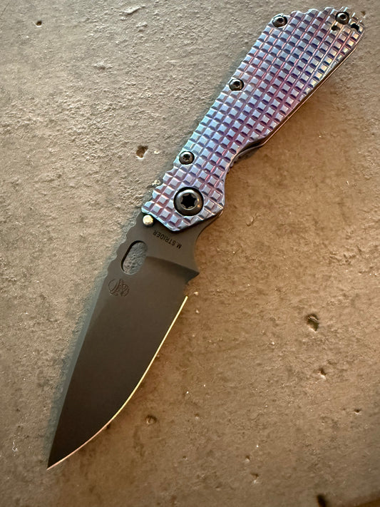 Strider SMF Monkey Edge FRAG CPM 3V spear point knife with blue and purple heat-anodized titanium presentation handle and dark blade.