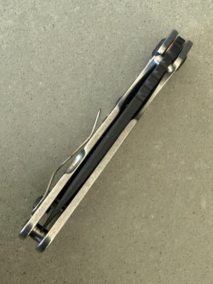 Strider SnG Battleship Blade Show West limited edition promotional image featuring black MagnaCut blade and laser camouflage titanium handle