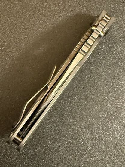 Strider SnG CC MagnaCut knife photographed from above showing contoured titanium handles, pocket clip, open-back construction and jimping.