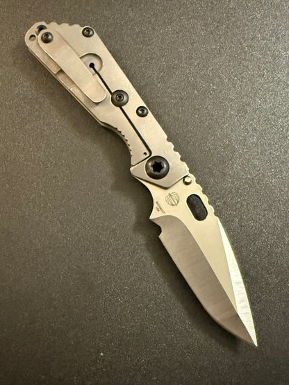 Strider SnG CC MagnaCut compound grind knife showing acid-washed titanium frame lock, titanium pocket clip and precision-ground blade.