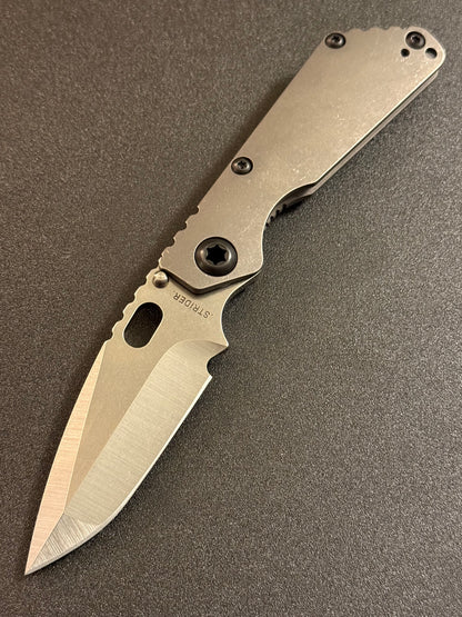 Strider SnG CC compound grind MagnaCut knife with acid-washed contoured titanium handle and black pivot hardware.