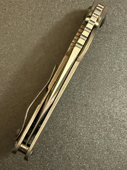 Strider SnG CC full Acid Bronze titanium folding knife showing handle spine, pocket clip, standoffs, and jimping.